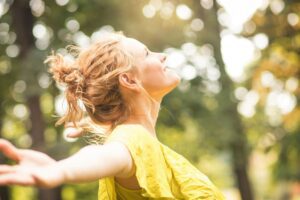 A woman lifting her face toward the sun with her arms open, symbolising personal transformation in this Tess René Coaching article on breaking generational cycles.