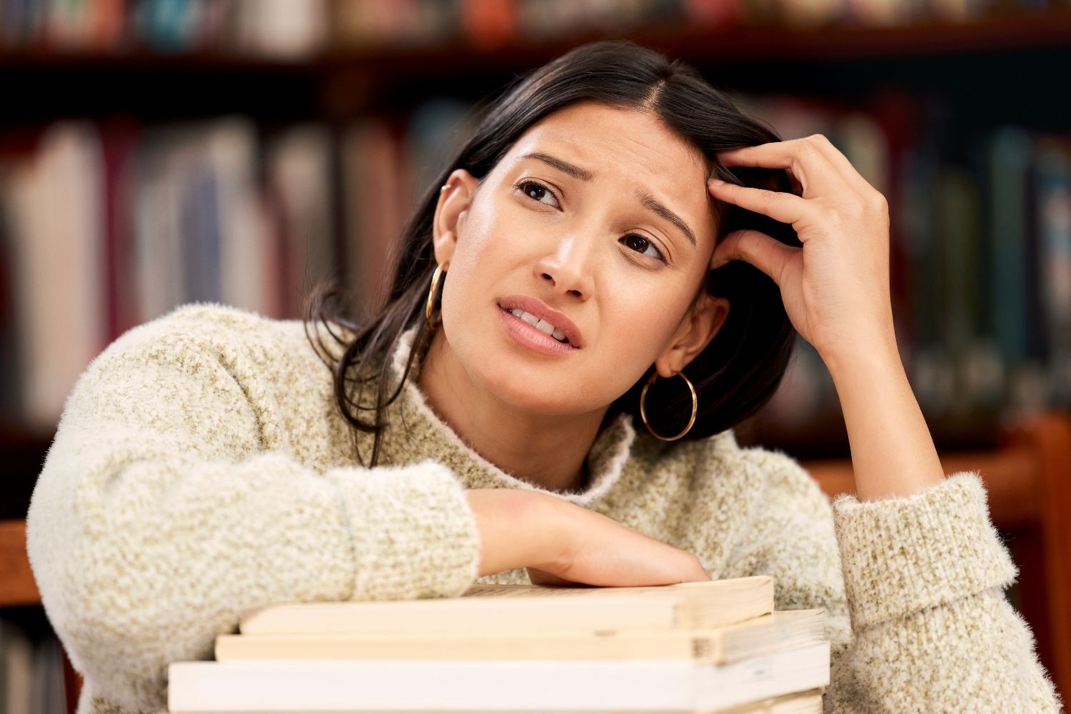 woman looking worried while leaning on stack of books stuck in analysis paralysis in a Tess René Coaching article on freezing in indecision and overanalyzing