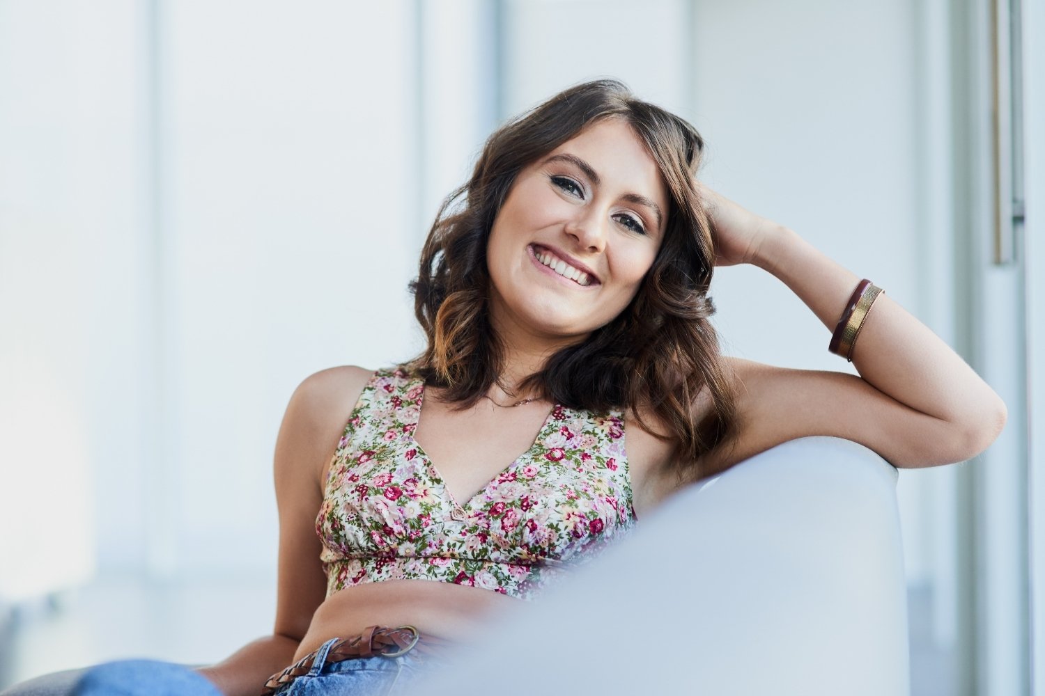 A woman smiling and relaxed on a sofa, representing how to be happy by yourself in this article by Tess Renè Coaching.