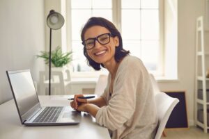 Smiling woman working at a laptop in this Tess René Coaching article about building success through clarity and confident decision making.