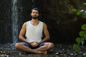 A man meditating near a waterfall, included in this Tess René Coaching article about somatic awareness during emotional memories.