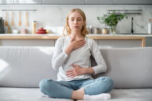 Woman with hands on chest and belly during grounding, shown in this Tess Renè Coaching article how to live a happy life.