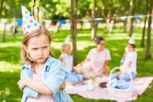 An upset child standing apart from others at a party, used in an article by Tess Renè Coaching about early relationship boundaries.