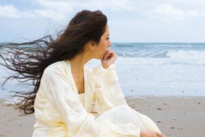 Woman sitting by the ocean looking thoughtful in this Tess René Coaching article about learning from mistakes and finding success.