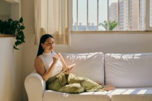 Woman journalling on a couch while reflecting on loneliness and aloneness in an article by Tess Renè Coaching.