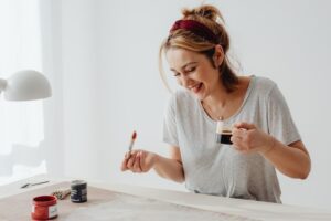smiling woman holding a paintbrush and coffee cup in a Tess René Coaching article on analysis paralysis