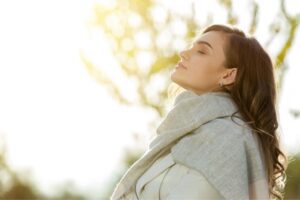 Woman breathing with eyes closed in sunlight, featured in a Tess Renè Coaching article on sensory grounding for joy.