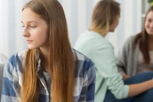 A teen looking away from a group, showing somatic signs of self-abandonment, featured in a Tess Renè Coaching article.