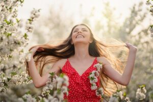 Woman smiling among blossoming trees in this Tess Renè Coaching article about rebuilding your capacity for joy.
