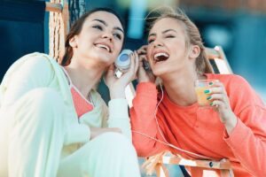 communication breakdown in friendships, two friends listening to music together, symbolizing a one friend is hearing something different than the other in this Tess Renè Coaching article