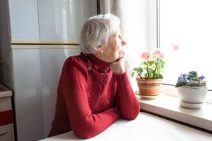 an older woman looking out a kitchen window symbolizing acceptance and grieving friendship loss without blame, in this Tess Renè Coaching article