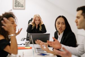 tense office meeting showing pressure from workplace culture that doesn't support each other's limits, in this Tess Renè Coaching article