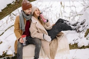 couple sitting together in the snow laughing in this Tess René Coaching article about moving from people pleasing into safer connection