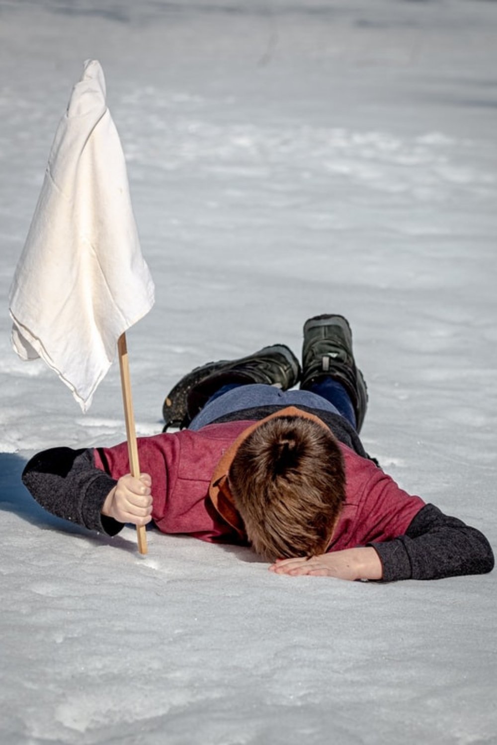 Child lying face down on frozen ice holding a white flag, symbolising exhaustion from trying too hard, featured in a Tess René Coaching article about healthy daily routines