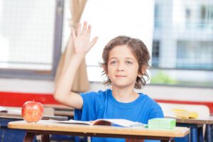 child calmly raising hand to speak in class in this Tess René Coaching article about stating boundaries kindly and respectfully