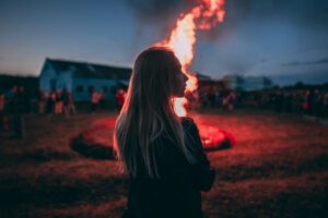 Woman standing alone watching a bonfire in the distance, pictured in this Tess René Coaching article about helping others too much