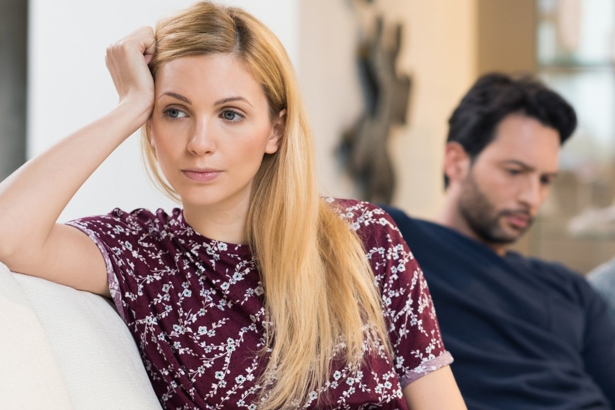 Overthinking relationships in a Tess René Coaching article, woman looking worried while partner sits behind her on the sofa