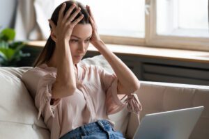 woman holding her head while looking uneasy in this Tess René Coaching article on anxiety triggered by saying no