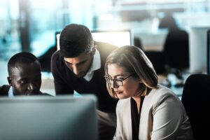 Woman working at a computer while colleagues lean in for help, pictured in this Tess René Coaching article on helping others
