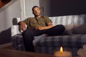 man sitting alone on a couch in a dim room, looking inward and withdrawn, shown in this Tess René Coaching article