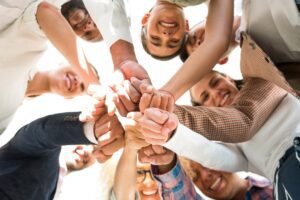 group of people standing in a circle with hands stacked together, representing early belonging and acceptance, in this Tess René Coaching article