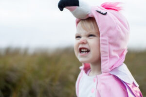 young child wearing a pink flamingo costume scrunching their face in frustration outdoors, showing a strong emotional reaction in this Tess Renè Coaching article on hidden emotional triggers