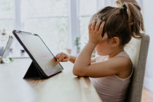 child sitting at a table with a tablet while holding her head in frustration, included in this Tess Renè Coaching article on why emotions can feel strong