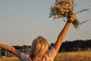 Woman holding flowers in the air symbolizing hope in this Tess René Coaching article about beginning again, personal growth, and living with purpose