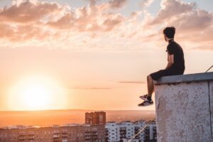 Person sitting alone on rooftop at sunset overlooking city buildings and glowing sky in this Tess Renè Coaching article about rebuilding joy and changing emotional attention