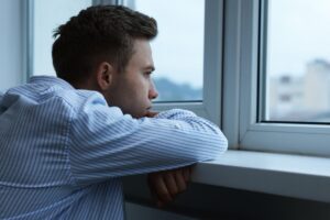 Man staring out a window symbolizing the frustration of waiting to live his life in this Tess René Coaching article about feeling lost in life and postponing happiness
