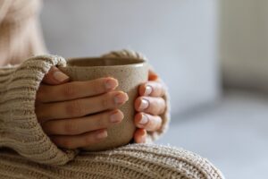 Hands wrapped around a warm mug in this Tess Renè Coaching article about emotional pain and nervous system overwhelm