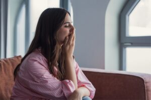 woman sitting on a couch with her hand over her mouth in Tess René Coaching article about emotional overwhelm and exploring the question: why am I so sensitive