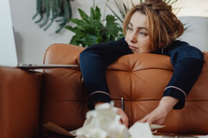 red-haired woman leaning on a couch beside a laptop and tissues looking tired in Tess René Coaching article about working with sensitivity