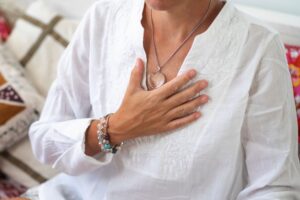 Person resting one hand on their chest while wearing a heart shaped pendant in a Tess René Coaching article section about building self trust, self compassion, and emotional safety