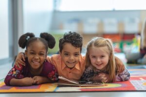 hree children smiling together with their arms around each other in a Tess René Coaching article section about keeping the peace, belonging, early beliefs, and self worth