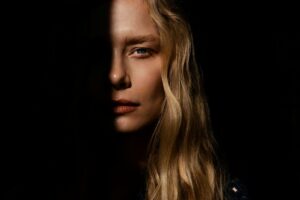 Close portrait of a blonde woman with half her face hidden in deep shadow, representing self criticism, shame, and the parts of yourself you struggle to accept.